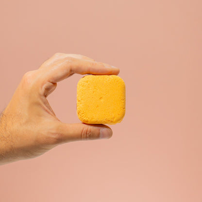 Hand holding a yellow bar of soap against a beige background