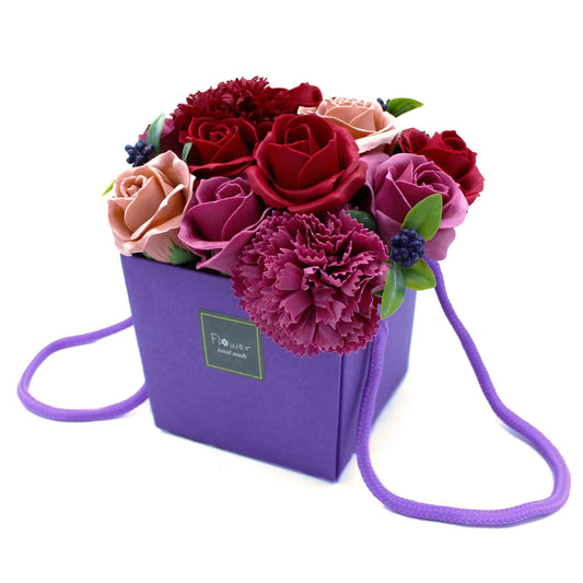 Floral arrangement in a purple box with a strap on a white background