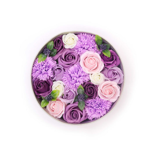 Round arrangement of purple, pink, and white flowers in a box on a white background