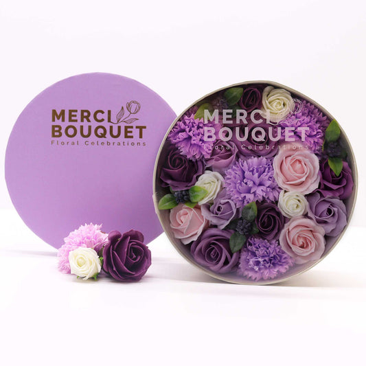 Floral arrangement in a round transparent container with 'Merci Bouquet' branding on a white background