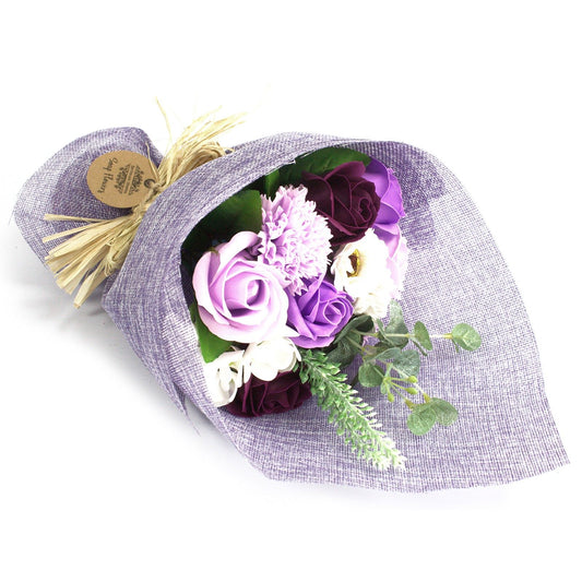Bouquet of purple and white flowers wrapped in gray paper with a gold bow on a white background