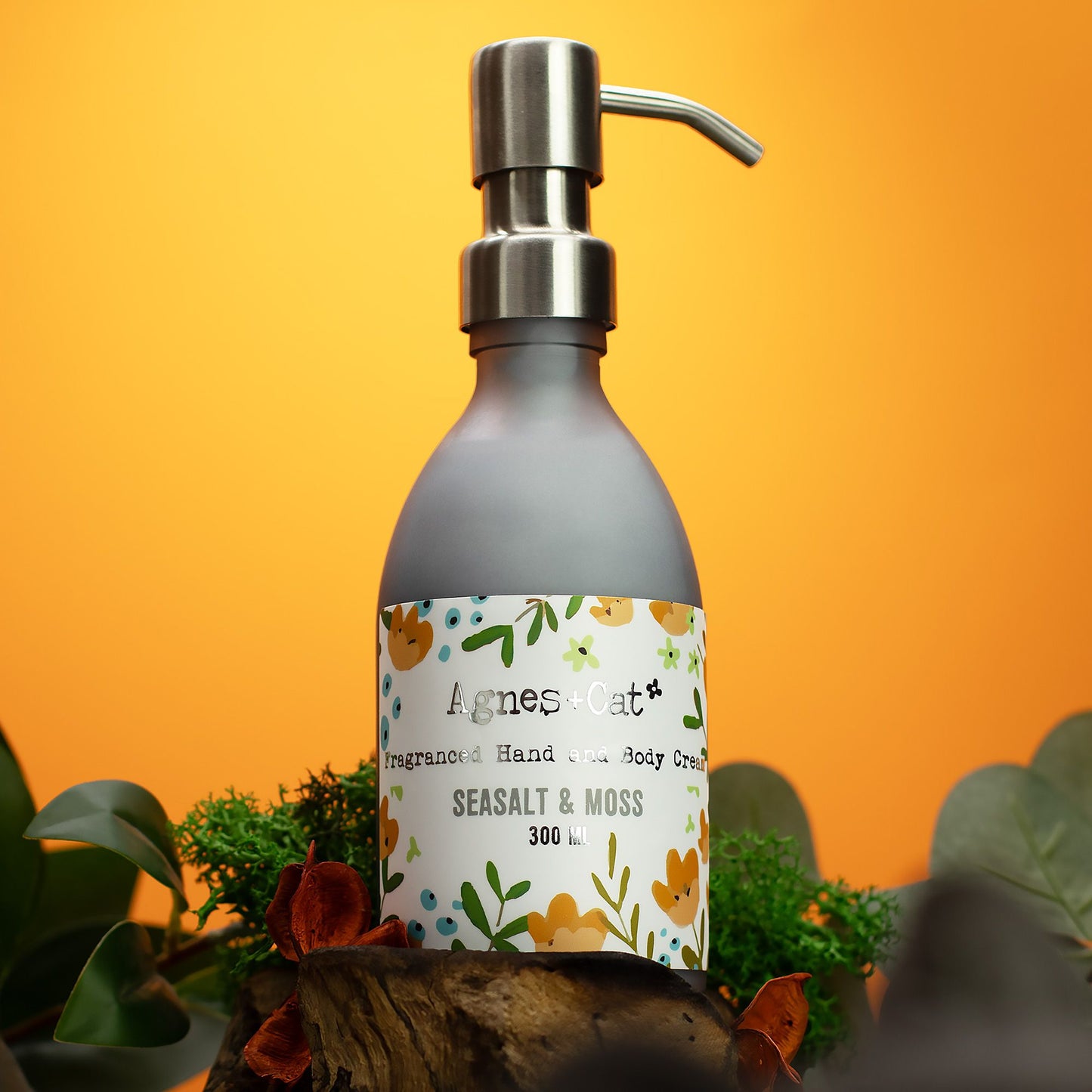 Bottle of Agnes & Co. hand and body cream with a pump on an orange background