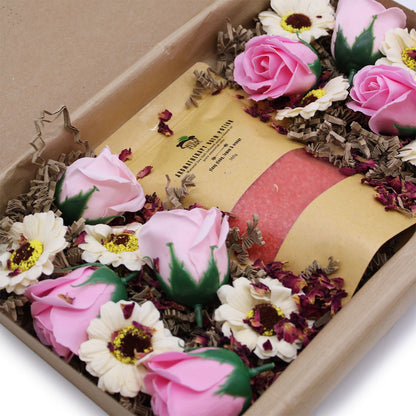 Bottle of perfume surrounded by pink and white flowers in a decorative box.