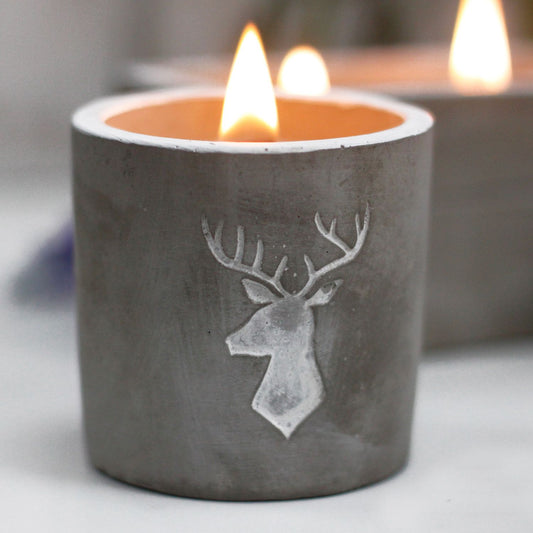 Cement candle holder with deer design and lit candle inside on a neutral background