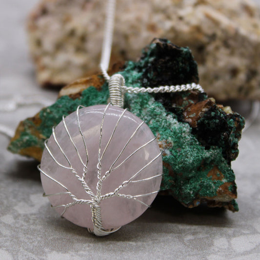 Necklace with a pink stone pendant featuring a silver tree design on a rock background