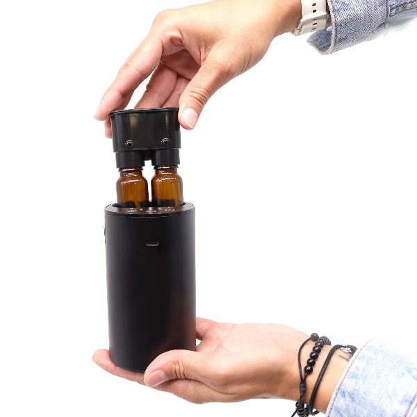 Person holding a black essential oil diffuser with two bottles inside on a white background
