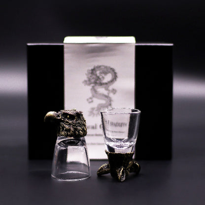 Two shot glasses with decorative stands in front of a branded box on a dark background