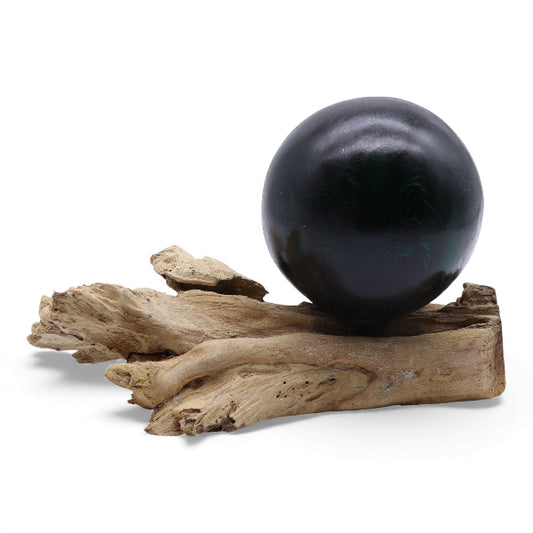 Black sphere on a piece of driftwood against a white background