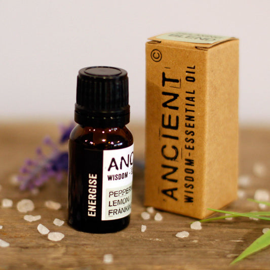 Bottle and box of Ancient Wisdom essential oil on a wooden surface with flowers in the background