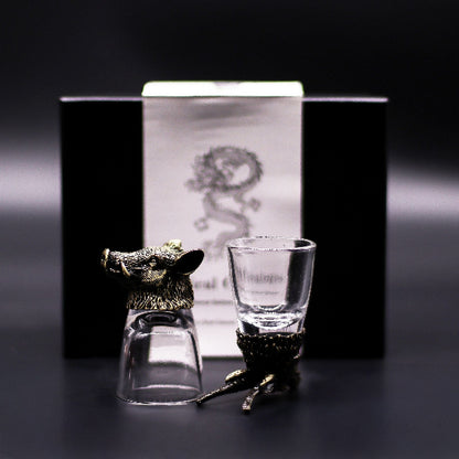 Two glass shot glasses with animal-shaped holders in front of a branded box on a dark background