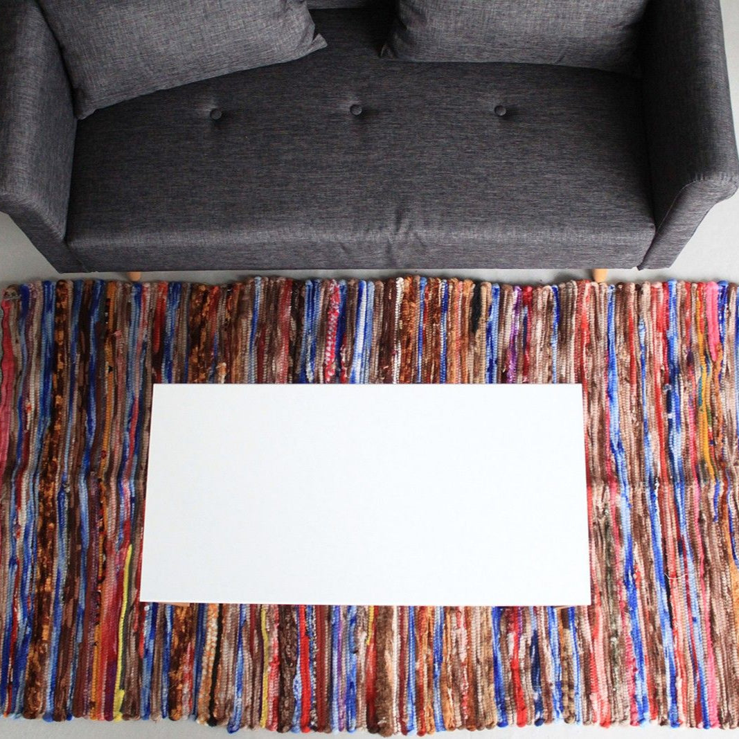 Multicolored woven rug with a white card on top, placed in front of a gray sofa.