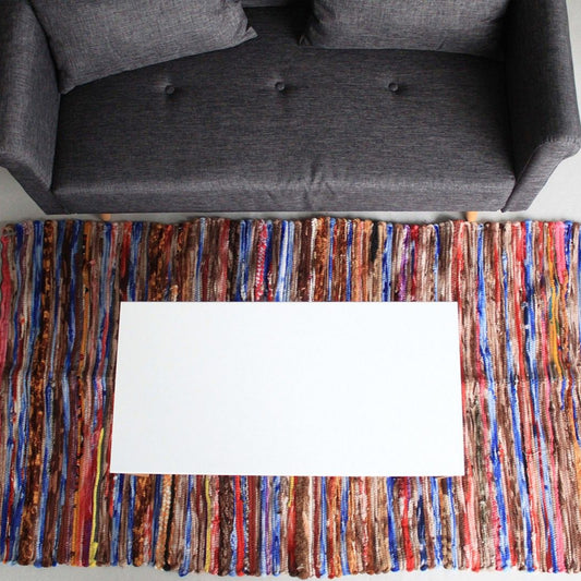 Multicolored woven rug with a white card on top, placed in front of a gray sofa.