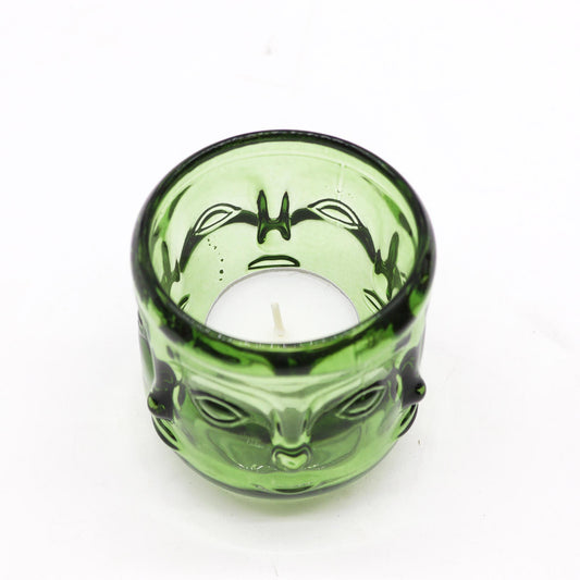 Green glass candle holder with buddha face design on a white background