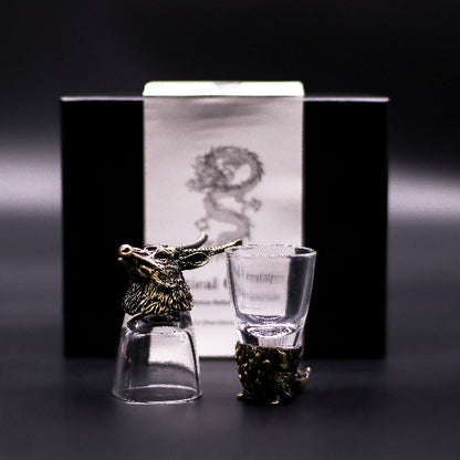 Two glass shot glasses with bronze deer heads on a dark background
