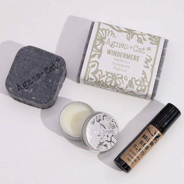 Collection of Agnes + Cat products including a bar of soap, a candle, and a rollerball on a white background.