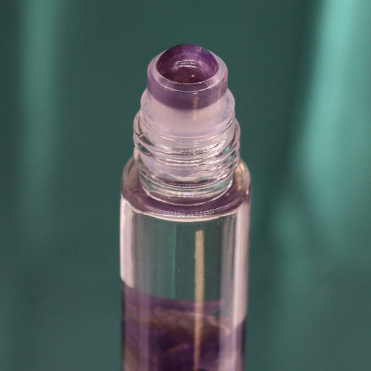 Roll-on bottle with purple cap and clear body on a green background