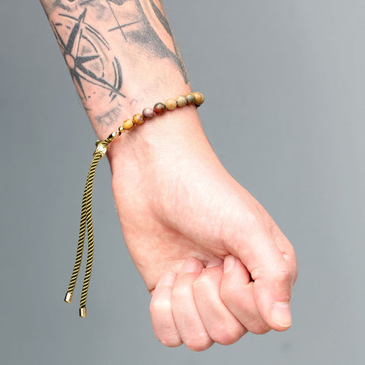 Hand wearing a beaded bracelet with a gold tassel on a gray background