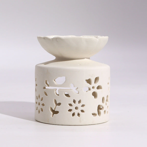 White ceramic oil burner with floral cutout design on a light gray background