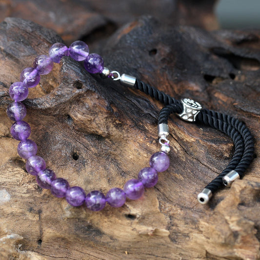 Purple beaded bracelet with black cord on a wooden surface