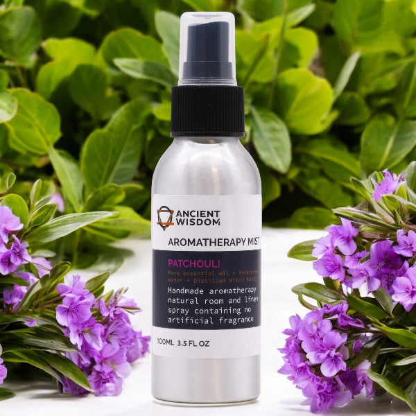 Aromatherapy mist bottle with patchouli scent surrounded by purple flowers and green leaves.