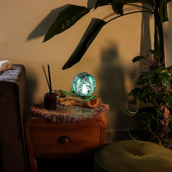 Decorative lamp on a wooden surface with plants and a couch in the background