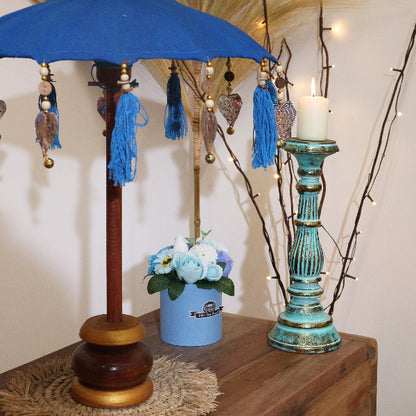 Decorative umbrella with tassels on a wooden stand, next to a blue vase with flowers and a teal candle holder.