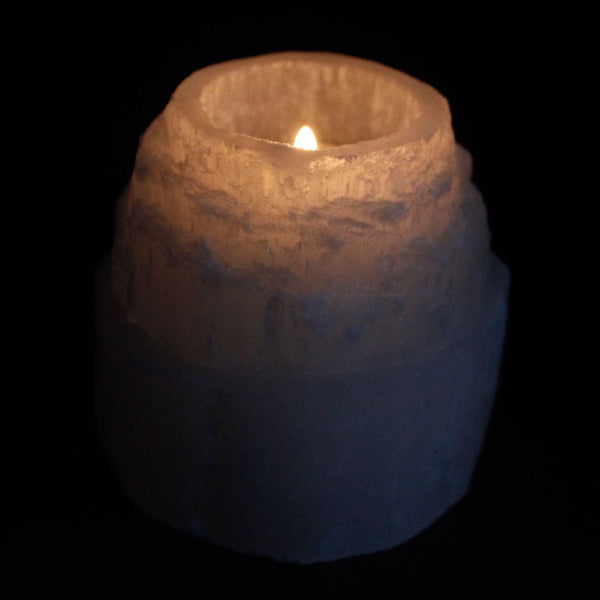 Candle in a textured ceramic holder on a black background