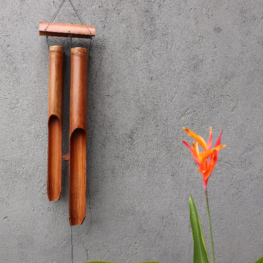 Wooden wind chime hanging on a gray wall with a red flower in the foreground.