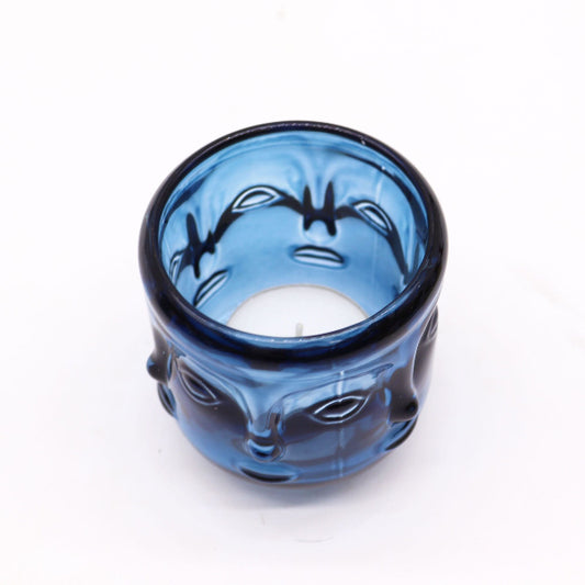 Blue glass candle holder with face design on a white background