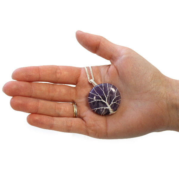 Hand holding a purple pendant necklace on a white background