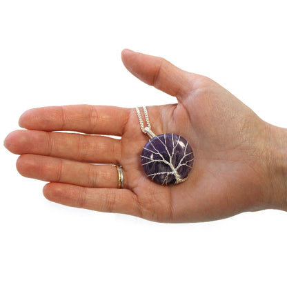 Hand holding a purple pendant necklace on a white background