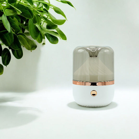 Small cylindrical humidifier with rose gold accents on a white surface with a plant in the corner.