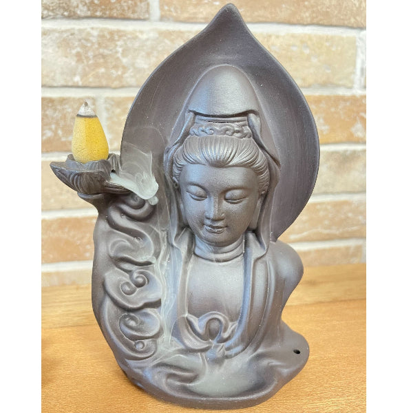 Statue of a seated figure with a lamp on a wooden surface and brick wall background