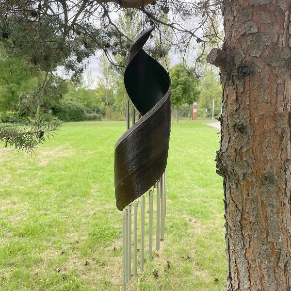 Decorative metal sculpture hanging from a tree in a park setting