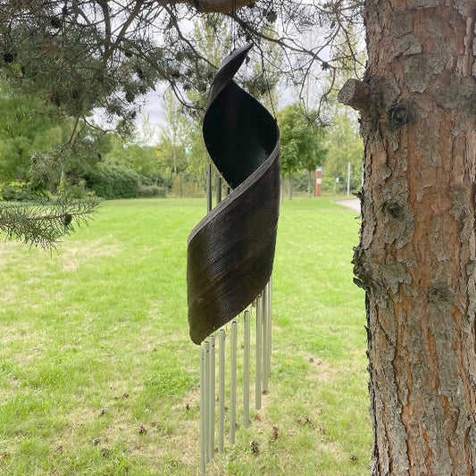 Decorative metal sculpture hanging from a tree in a park setting