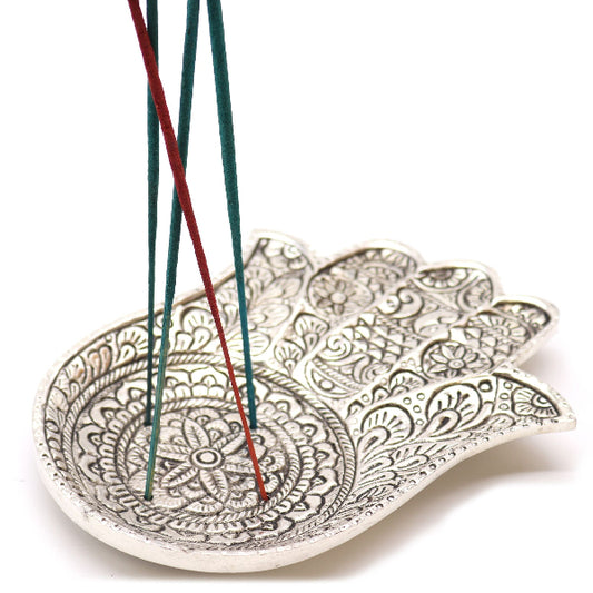Decorative leaf-shaped incense holder with intricate patterns holding incense sticks on a white background