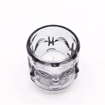 Clear glass candle holder with a face design on a white background