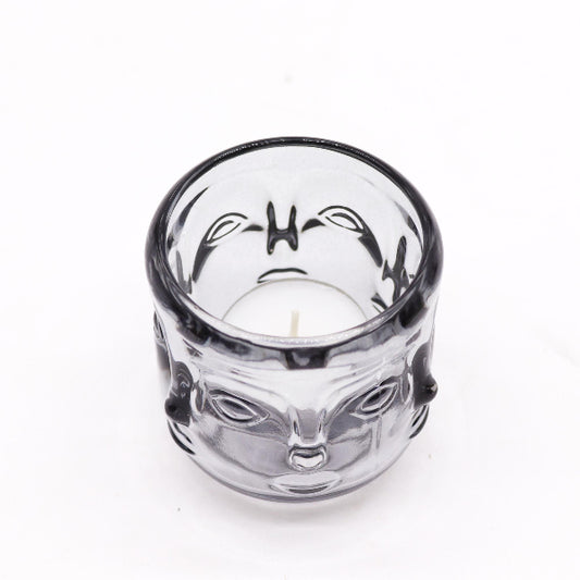Clear glass candle holder with a face design on a white background