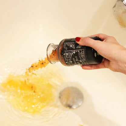 Hand holding a bottle over a sink with soap suds