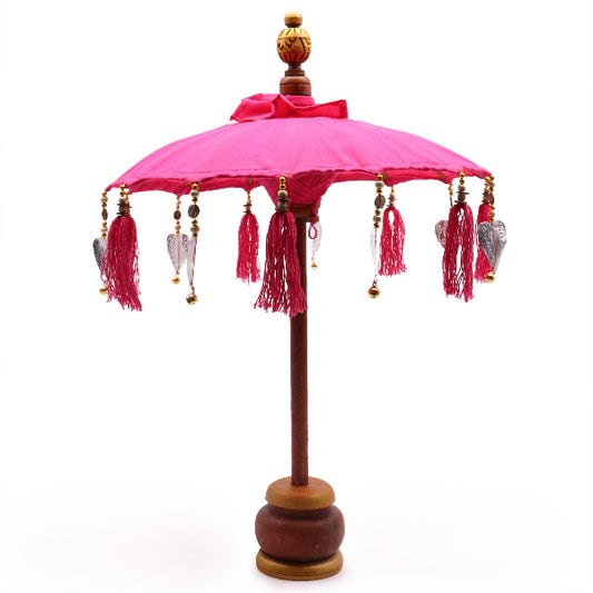 Decorative pink umbrella with tassels and wooden base on a white background