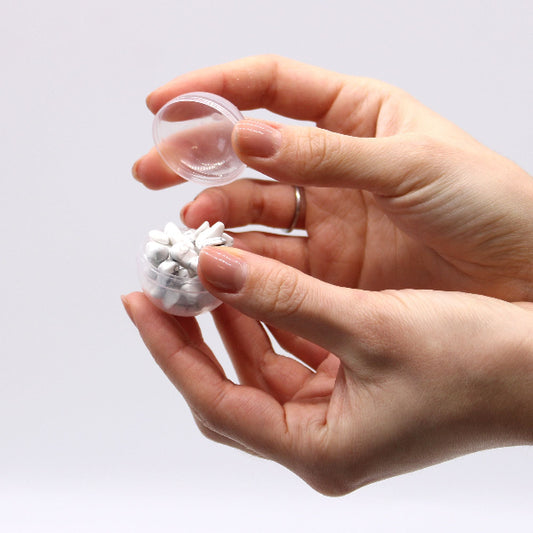 Hand holding a small transparent container with white beads against a light gray background