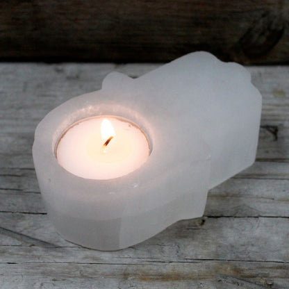 Tealight candle in a white stone hamsa holder on a wooden surface