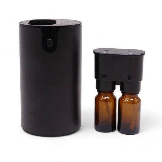 Black cylindrical diffuser with two amber glass bottles on a white background