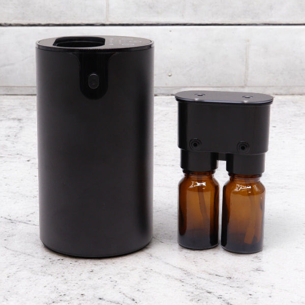 Black cylindrical diffuser and two amber bottles on a light wooden surface.
