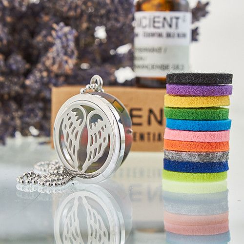 Silver locket with angel wings, colorful hair ties, and a bottle of essential oils on a reflective surface.