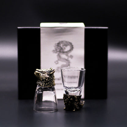 Two glass shot glasses with animal-shaped holders in front of a branded box on a dark background