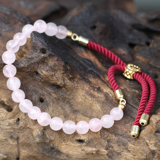 Rose quartz beaded bracelet with red cord and gold clasps on a wooden surface
