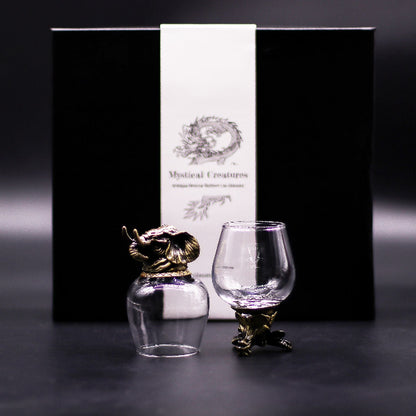 Two glass figurines with gold animal sculptures in front of a black box labeled 'Mystical Creatures'.