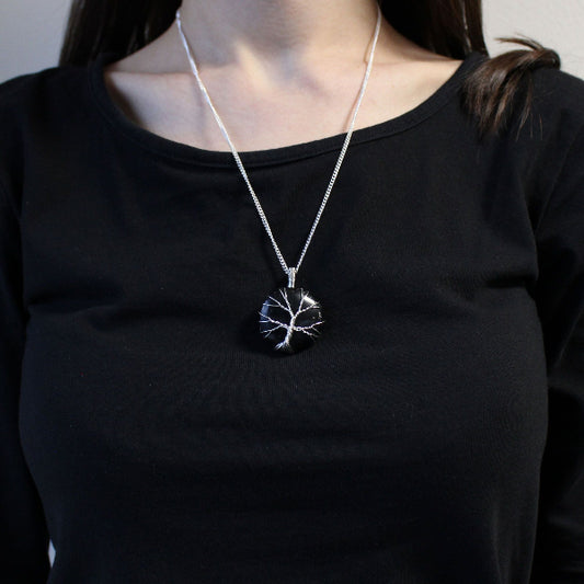 Person wearing a black shirt with a silver necklace featuring a tree pendant.