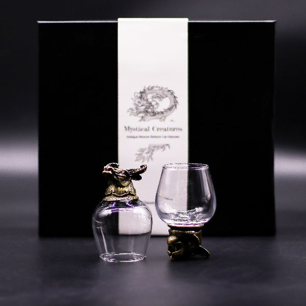 Two glass items with decorative bases in front of a black box with a white label.